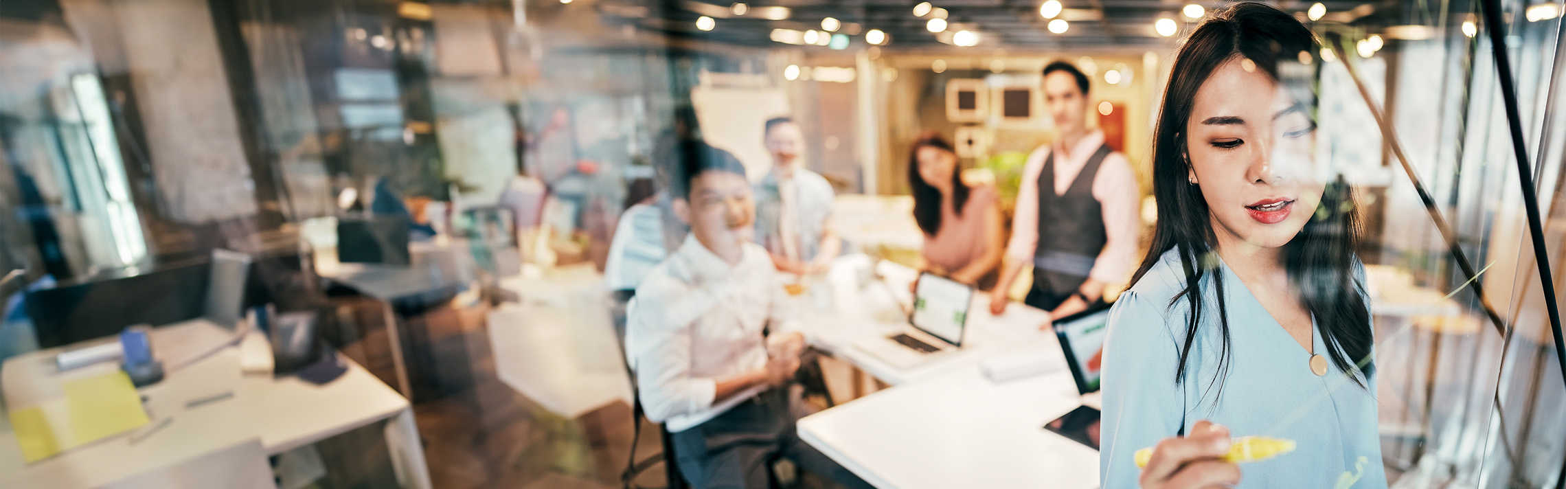 Woman writing on a board with co-workers sitting behind her